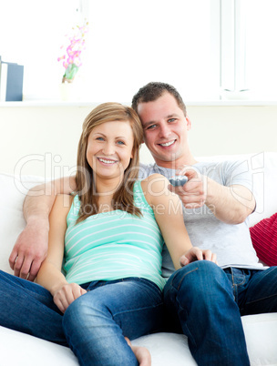 Glowing young couple sitting on the sofa watching tv