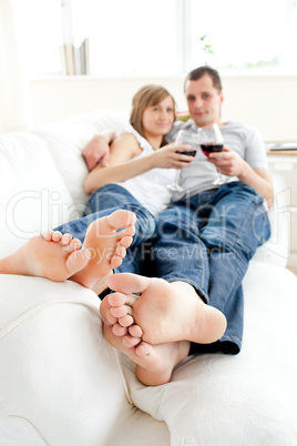 Caucasian young couple lying on the sofa drinking wine