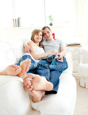 Happy young couple lying together on the couch watching televisi