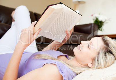 Positive young woman reading a book lying on the floor