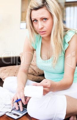 Depressed young woman using her calculator holding a bill