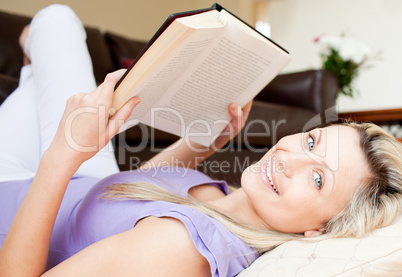 Charming young woman reading a book lying on the floor