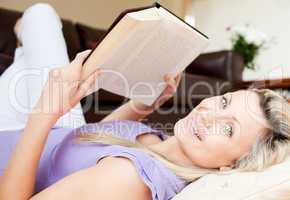 Charming young woman reading a book lying on the floor