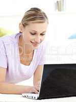 Attractive young woman using her laptop lying on the floor