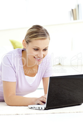 Radiant young woman using her laptop lying on the floor