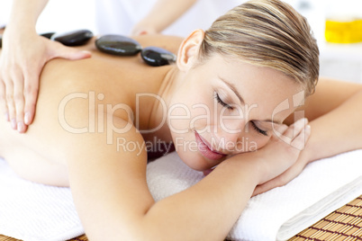 Bright young woman enjoying a back massage with hot stone