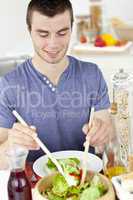 Attractive young man putting salad on a plate