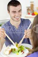 Happy  man putting salad on a plate having dinner with his girlf