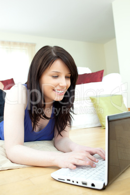 Bright female teenager using her laptop lying on the floor