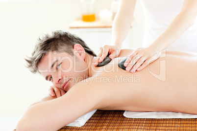 Charming young man receiving a back massage with hot stone