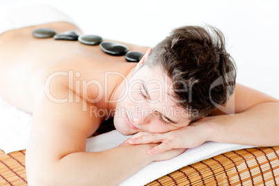 Resting young man lying on a massage table with hot stone on his