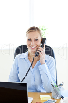 Charming young businesswoman talking on phone sitting at her des