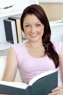 Smiling young woman reading a book on the sofa