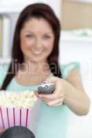 Bright caucasian woman holding a remote and popcorn in the living room