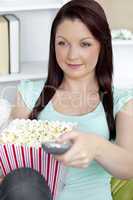 Bright caucasian woman holding a remote and popcorn in the living room