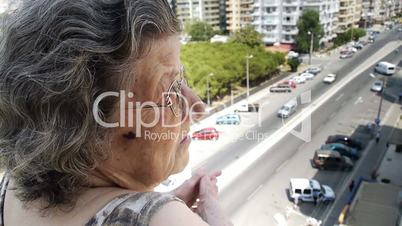 Old retired woman watching traffic from balcony