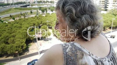 Old retired woman watching traffic from balcony