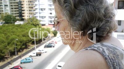 Old retired woman watching traffic through window