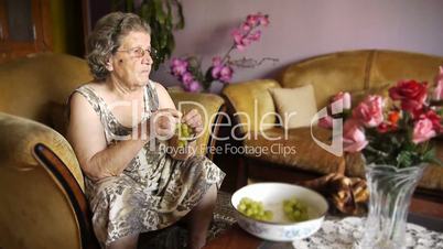 Old retired woman eating grapes in home