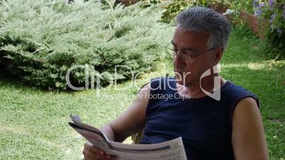 Old retired man reading newspaper outdoors
