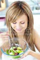 Pretty young woman eating a fruit salad in the kitchen