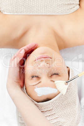 Relaxed young woman receiving white cream on her face