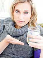 Sick depressed woman holding pills and water looking at the came