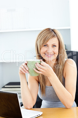 Attractive businesswoman holding a cup using her laptop