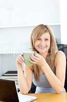 Attractive businesswoman holding a cup using her laptop