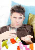 Sick caucasian man holding pills and water looking at the camera