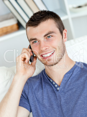 Charismatic young man talking on phone sitting on the sofa