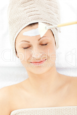 Resting young woman receiving white cream on her face