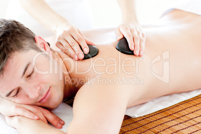 Positive young man enjoying a back massage with hot stone