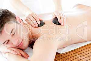 Positive young man enjoying a back massage with hot stone