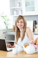 Smiling woman having breakfast in front of the laptop