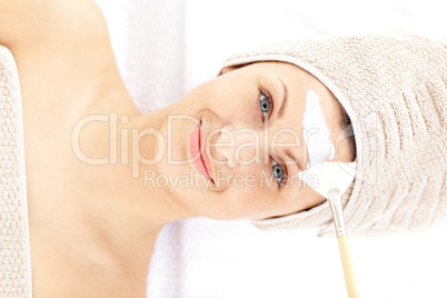 Pretty young woman receiving white cream on her face