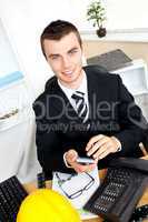 Positive businessman using his calculator looking at the camera