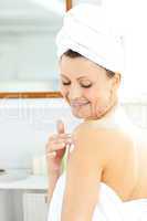 Merry young woman putting cream on her body wering a towel