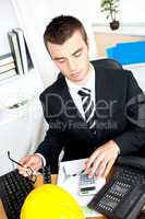 Serious young businessman using his calculator