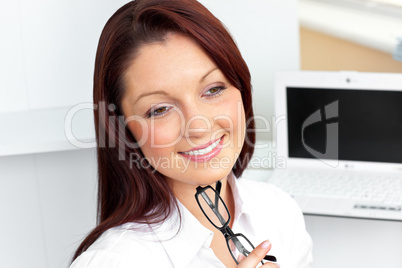 Confident businesswoman sitting in her office holding glasses