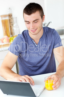 Charming young man using his laptop holding orange juice