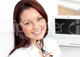 Charming businesswoman sitting in her office holding glasses