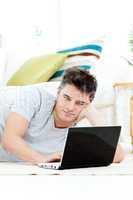 Charming young man using his laptop lying on the floor