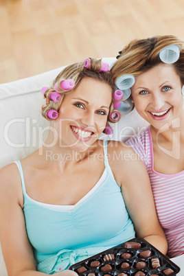 Delighted women wearing hair rollers eating chocolate looking at