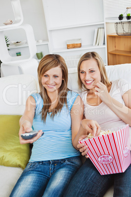Joyful female friends watching television and eating popcorn