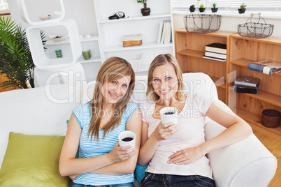 Relaxed two women drinking coffee smiling at the camera