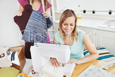 Happy woman sewing  in the kitchen with her friend