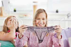 Laughing women holding lingerie sitting on the sofa