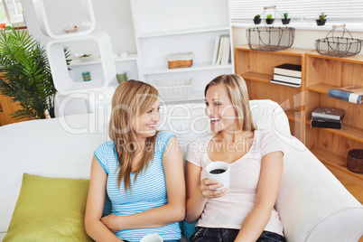 Cheerful two women drinking coffee and talking while sitting on