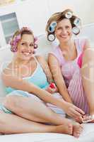 Cheerful female friends doing pedicure and wearing hair rollers